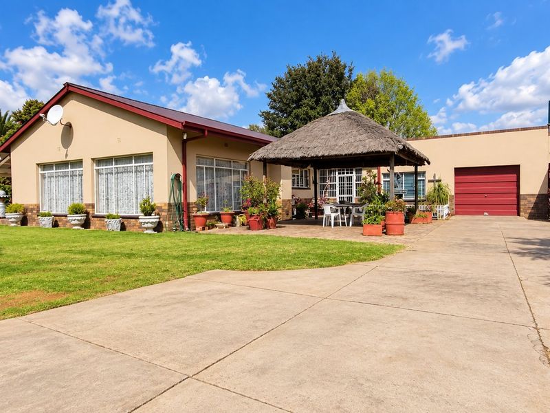 Rear view of the farm property featuring a thatched lapa, expansive concrete driveway, garage access, and a water storage tank.