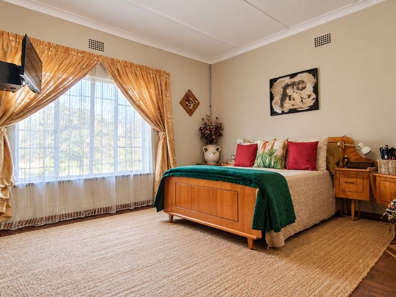A spacious bedroom featuring parquet flooring, a large window with security bars, and coved ceiling details, offering a comfortable and well-lit living space.