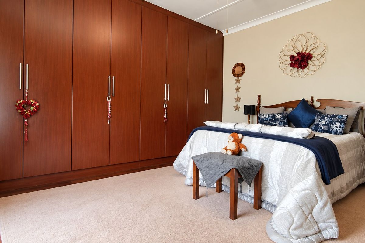 A spacious bedroom featuring extensive built-in floor-to-ceiling wooden wardrobes, neutral carpeting, and a coved ceiling.