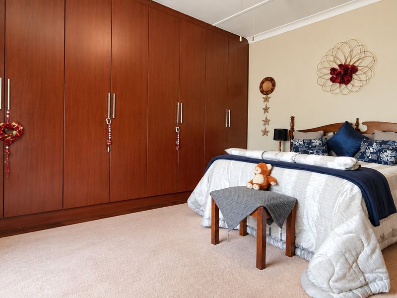 A spacious bedroom featuring extensive built-in floor-to-ceiling wooden wardrobes, neutral carpeting, and a coved ceiling.