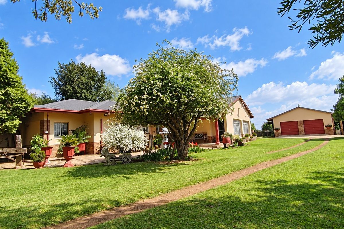 A well-maintained farm property featuring a spacious lawn, paved patio area, and a detached garage under a clear blue sky.
