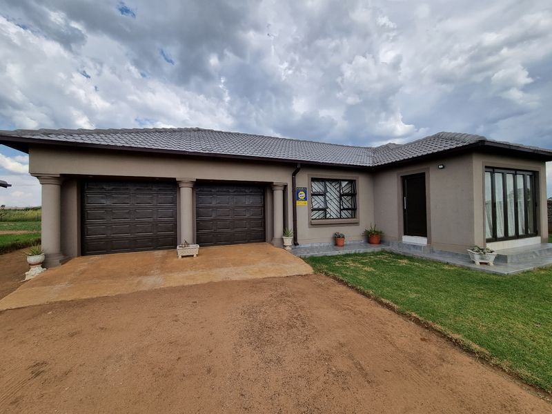 Front elevation of a modern single-story house featuring a double garage, tiled roof, and a paved entrance area with a well-maintained lawn.