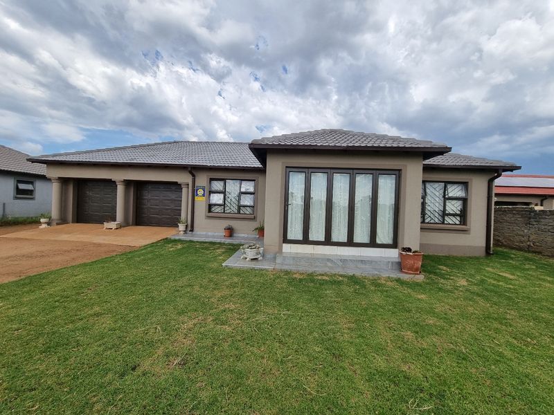 A well-maintained single-story house featuring a double garage, tiled roof, and a neat front lawn with paved access.