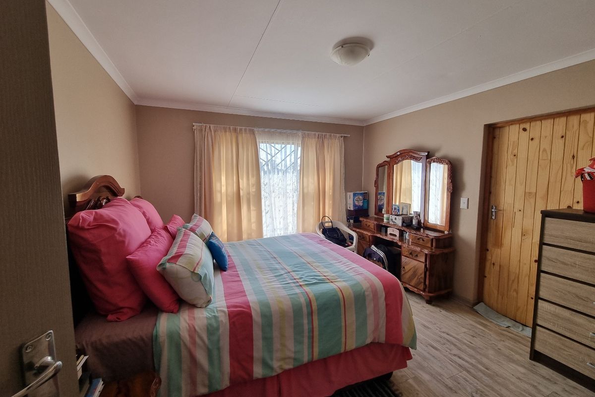A functional bedroom featuring laminate flooring, a timber door, and a security gate over the window, providing a comfortable and private living space.