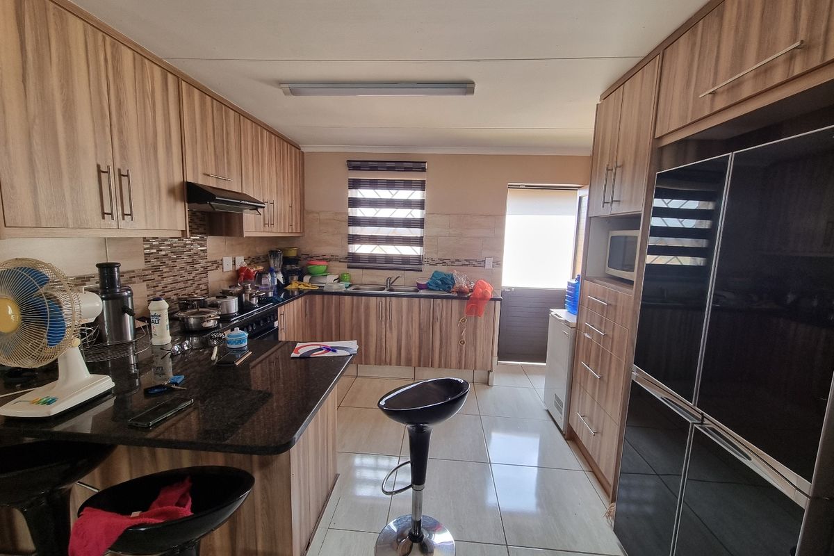 A functional kitchen featuring wood-look cabinetry, granite countertops, tiled flooring, and an integrated extractor fan with direct access to the exterior.