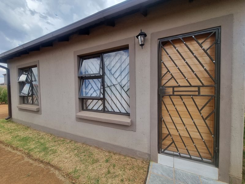 A well-maintained exterior facade featuring a modern security gate, top-hung windows, and a tiled entrance area.