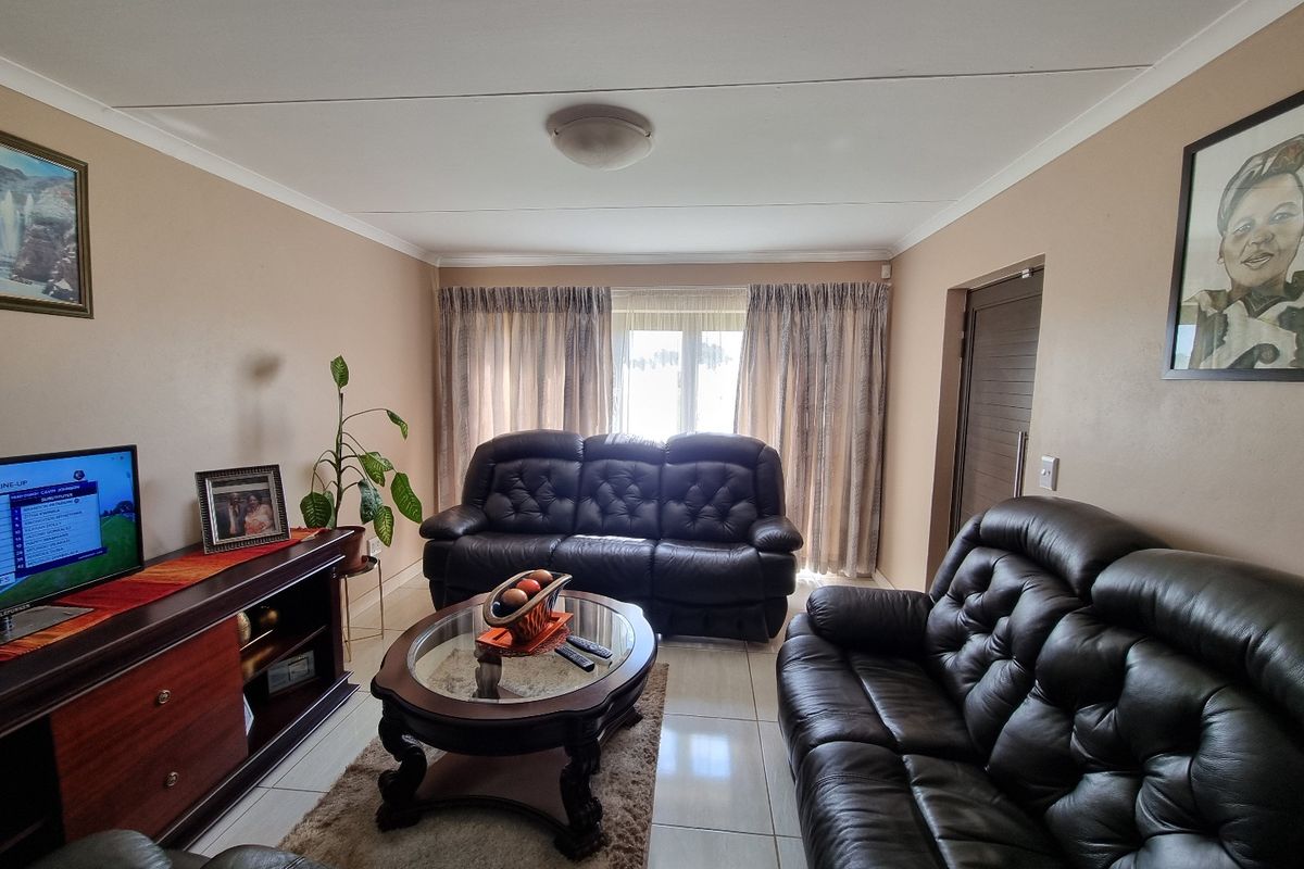 A comfortable living room featuring neutral wall tones, tiled flooring, and natural light through window curtains.