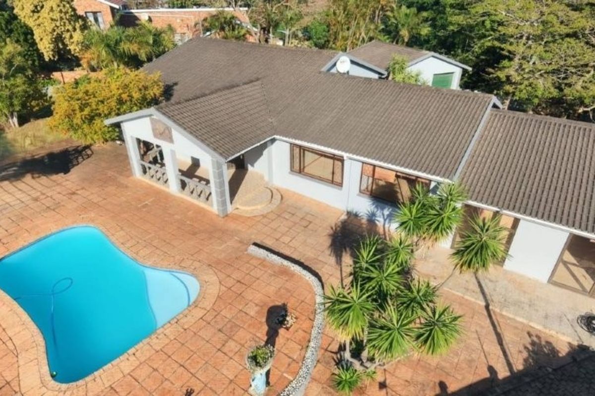 Aerial view of the property featuring a swimming pool, extensive paved patio area, and a covered veranda attached to the main house structure.