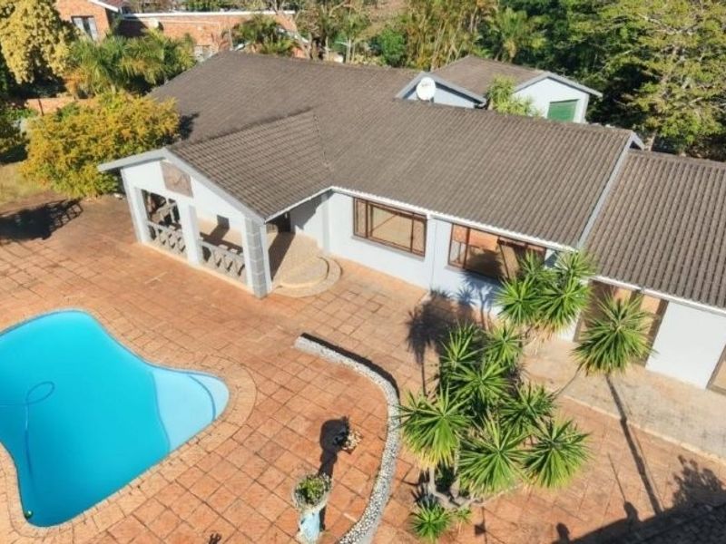 Aerial view of the property featuring a swimming pool, extensive paved patio area, and a covered veranda attached to the main house structure.
