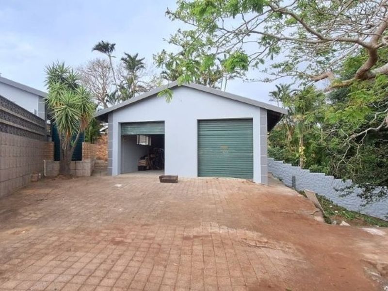 A detached double garage with roller shutter doors, featuring a paved driveway and surrounding boundary walls in a residential setting.