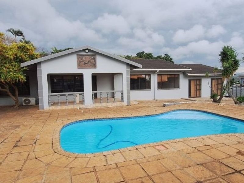 Rear exterior view featuring a swimming pool, paved patio area, and a covered veranda with balustrade detailing.