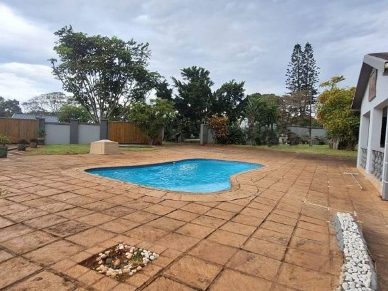 Outdoor pool area featuring a paved patio, swimming pool, and access to a covered veranda, set within a fenced garden.