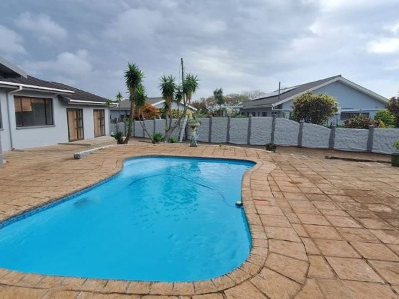 Outdoor pool area featuring a swimming pool, extensive paved patio space, and a secure precast concrete boundary wall.