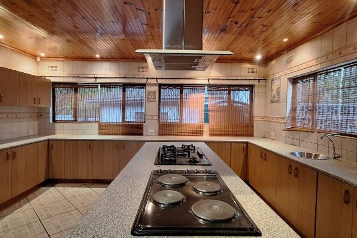 Spacious kitchen featuring a large central island with dual cooktops, extensive cabinetry, granite countertops, and a distinctive timber-paneled ceiling.