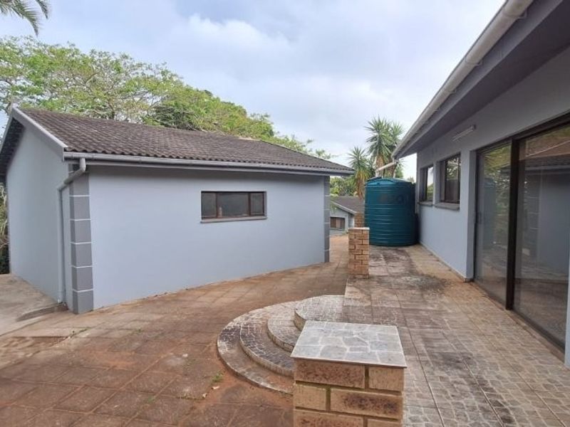 Rear exterior view showing a paved patio area, sliding door access, and a water storage tank adjacent to the main building structure.