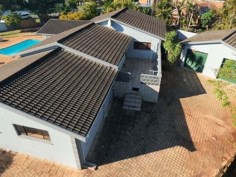 Aerial view of the property featuring a tiled roof house, paved driveway, double garage, and a swimming pool in the garden area.