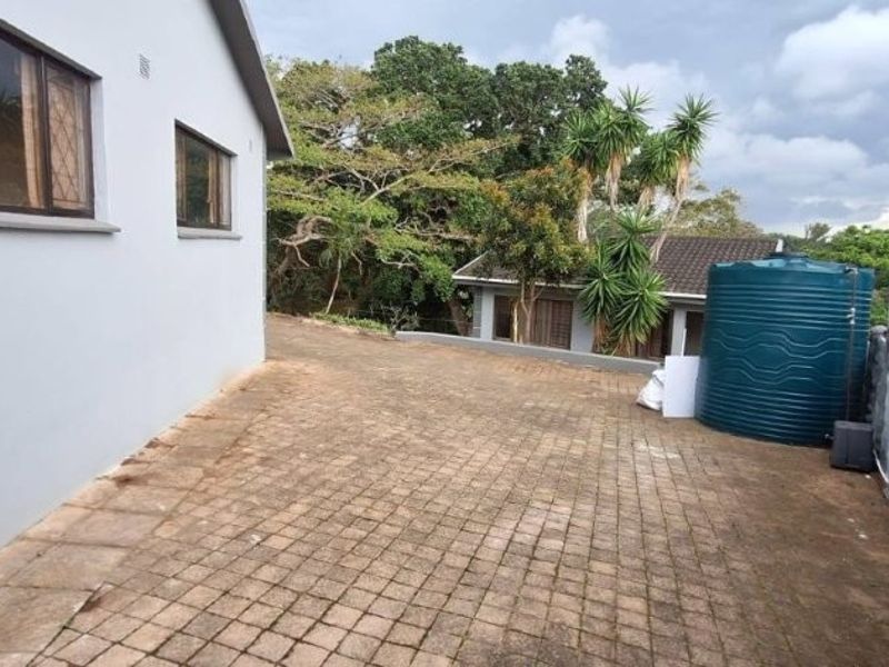 Rear exterior area featuring a paved driveway, water storage tank, and secure perimeter walling with electric fencing.
