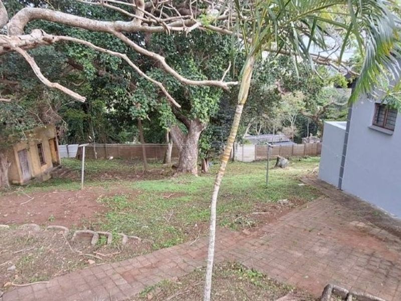 A view of the rear garden area featuring paved pathways, mature trees, and the side elevation of the house.