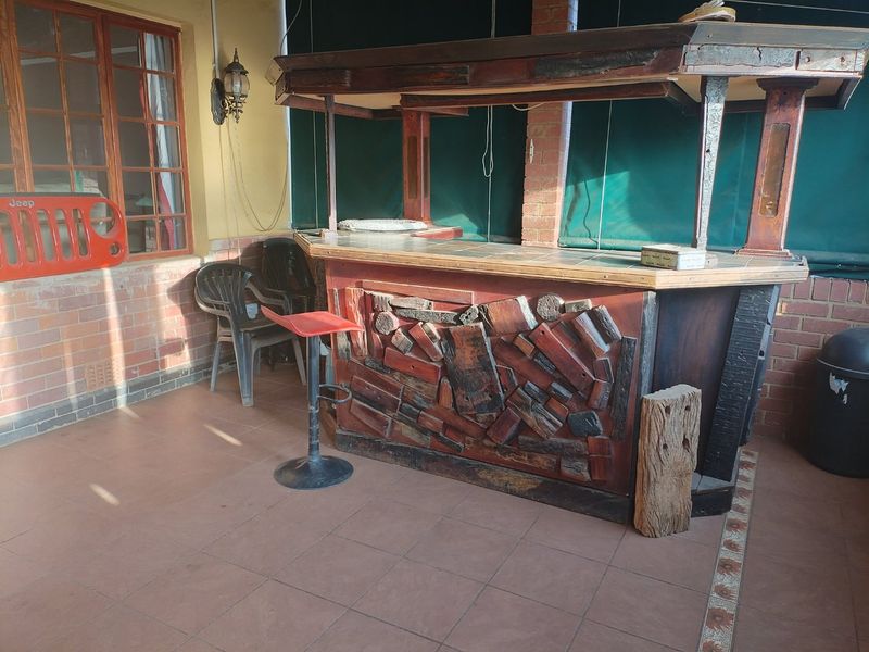 Covered patio area featuring a rustic built-in wooden bar, tiled flooring, and brick wall accents, suitable for outdoor entertaining.