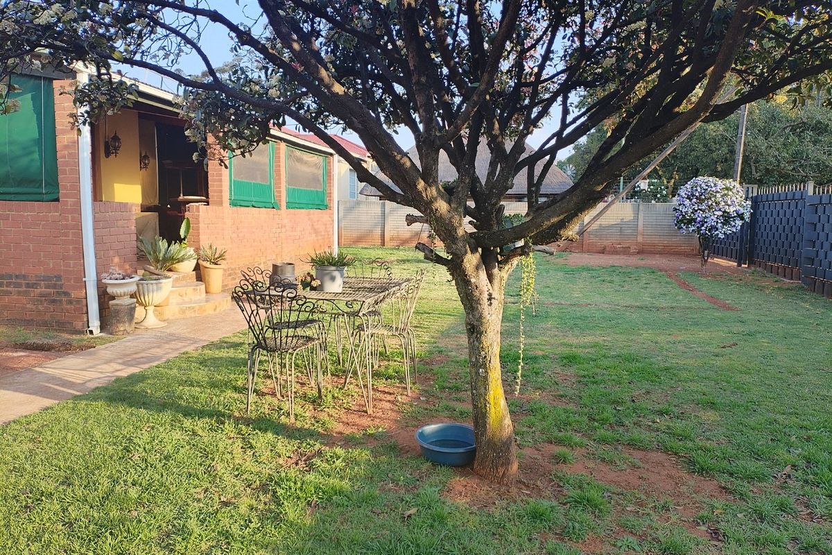 A spacious rear garden featuring a brick-faced home, a concrete patio area, and a well-maintained lawn enclosed by a perimeter wall.