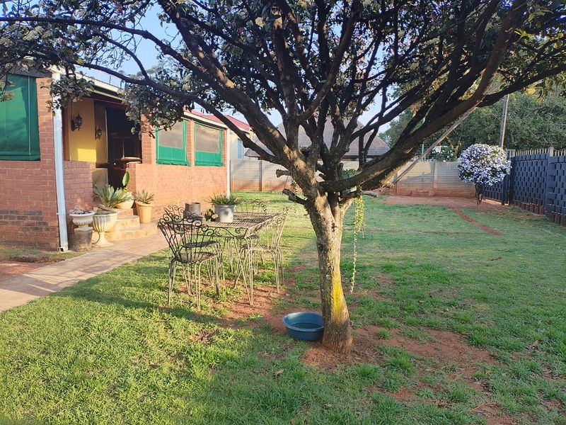 A spacious rear garden featuring a brick-faced home, a concrete patio area, and a well-maintained lawn enclosed by a perimeter wall.