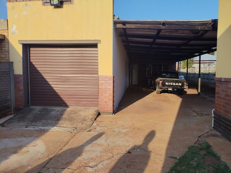Exterior view of a property featuring a single roller shutter garage door and an attached carport with a concrete driveway.