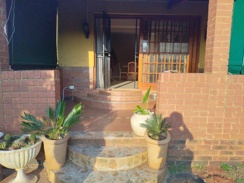 A covered brick patio featuring tiled steps leading to a timber-framed glass entrance door with security gate.