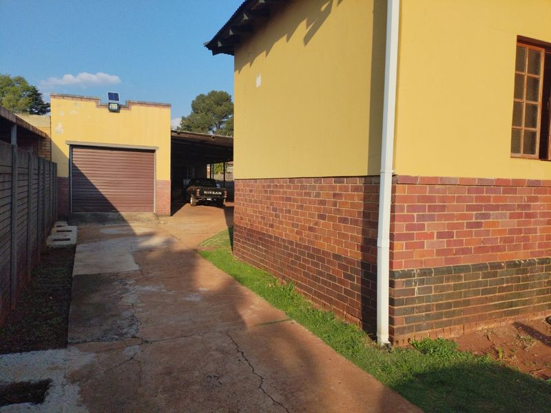 Rear exterior view showing a brick and plaster house facade, concrete driveway, and a detached garage structure.