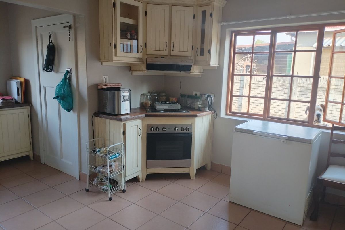 A functional kitchen featuring cream-colored built-in cabinetry, a corner oven and hob setup, and tiled flooring with natural light from the window.