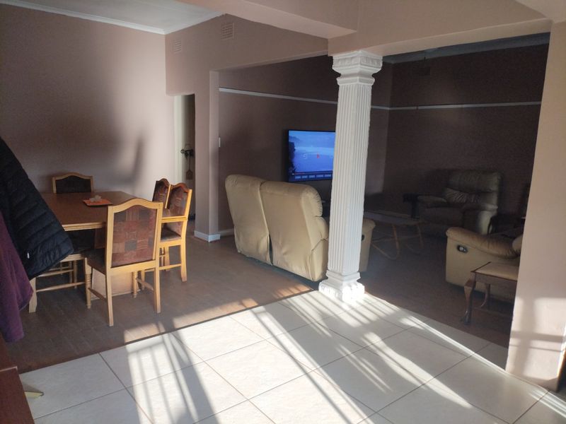Open-plan living and dining area featuring a decorative column, mixed flooring types, and coved cornicing, providing a versatile space for family living.