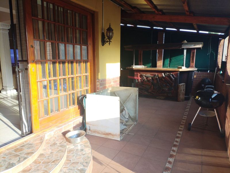 A covered patio area featuring a built-in bar, tiled flooring, and timber-framed sliding doors providing access to the interior living space.