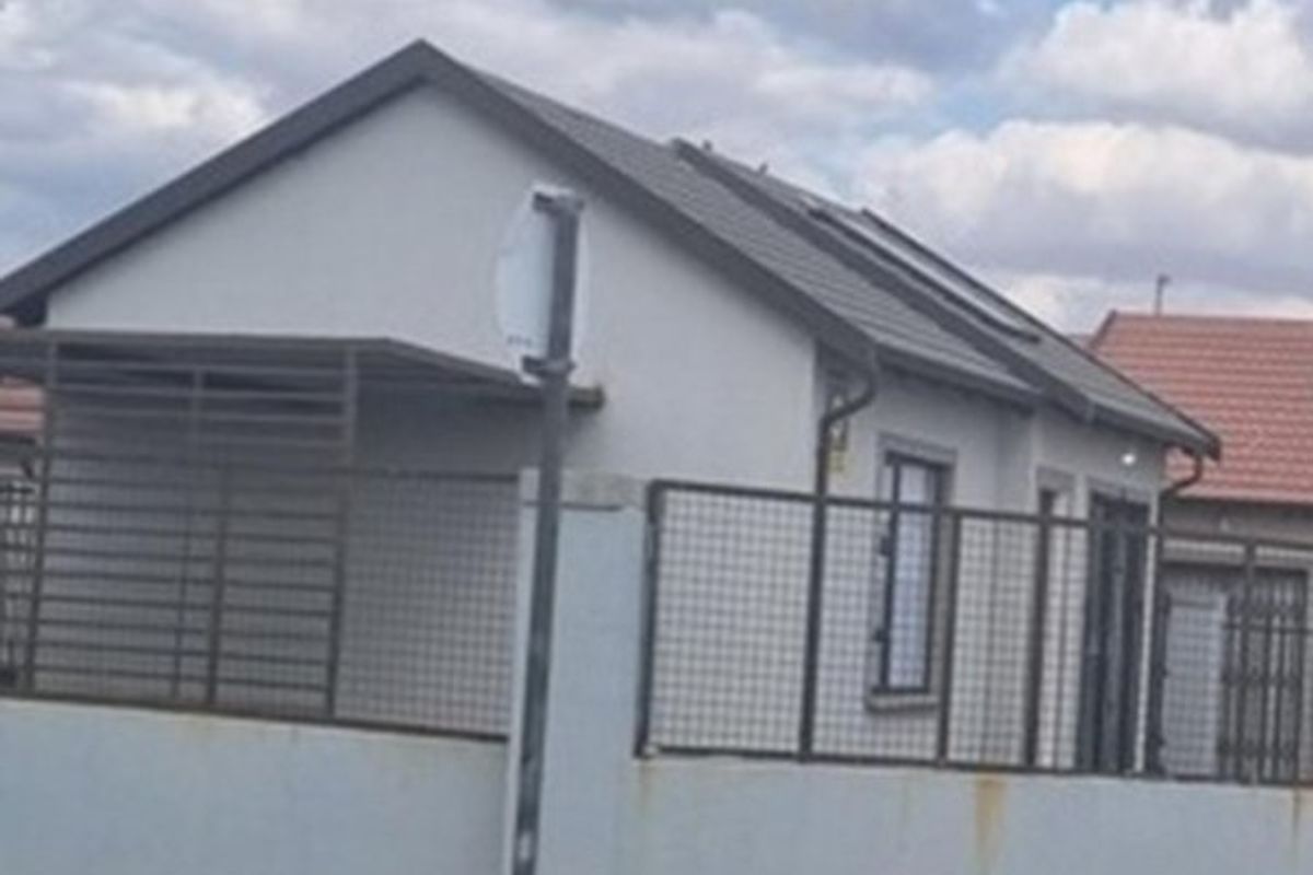 Front view of a single-story residential property featuring a tiled roof, plastered exterior walls, and metal perimeter fencing with an integrated carport.