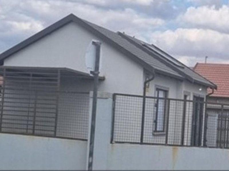 Front view of a single-story residential property featuring a tiled roof, plastered exterior walls, and metal perimeter fencing with an integrated carport.