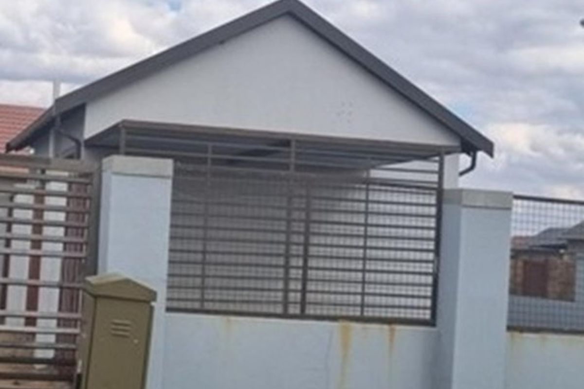 Front view of the property featuring a gabled roof structure, perimeter wall with metal security fencing, and a post box.