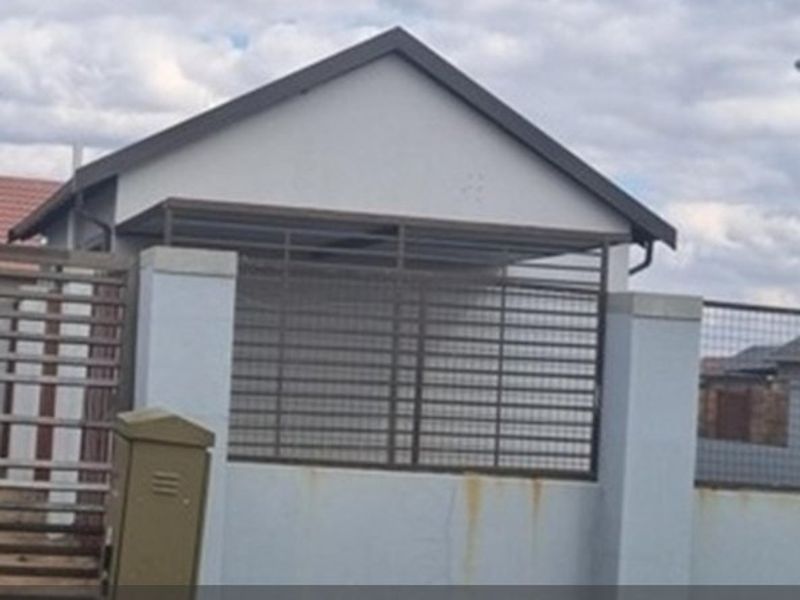 Front view of the property featuring a gabled roof structure, perimeter wall with metal security fencing, and a post box.