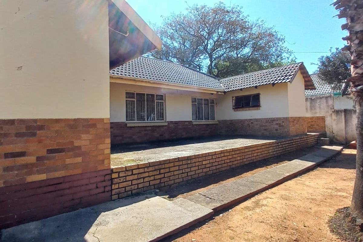 Rear view of the house featuring a brick facade, tiled roof, and a spacious concrete patio area in the backyard.