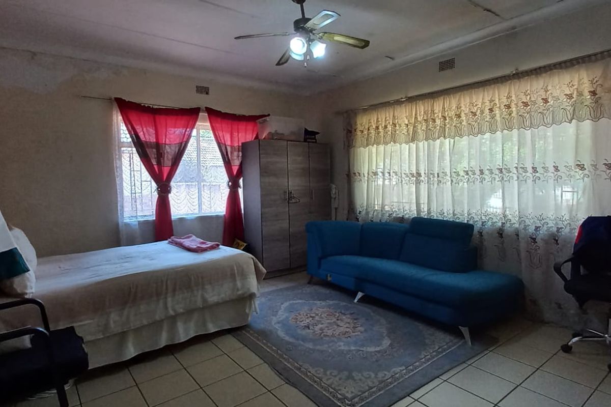 A bedroom featuring tiled flooring, a ceiling fan, and security bars on the windows, showing signs of wear on the walls and ceiling.
