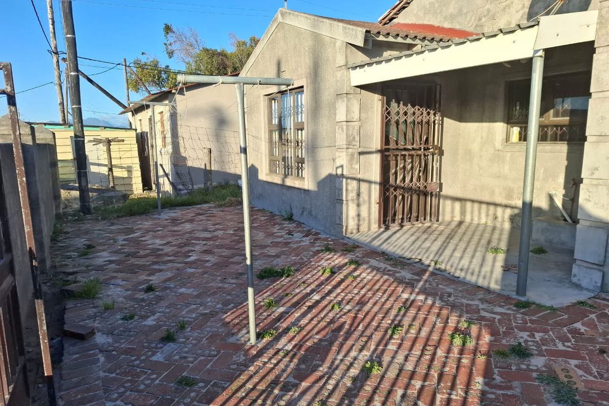 Rear exterior view of the property featuring a brick-paved courtyard, a covered patio area, and a security gate.