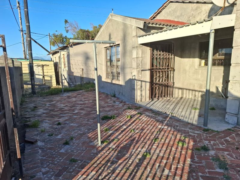 Rear exterior view of the property featuring a brick-paved courtyard, a covered patio area, and a security gate.