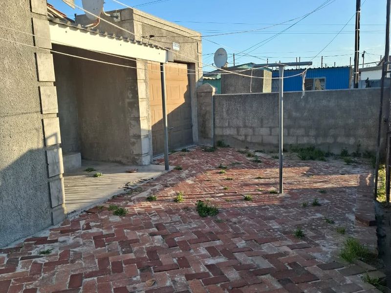 Rear exterior area featuring brick paving, a covered patio space, and a boundary wall, offering potential for outdoor improvement and landscaping.