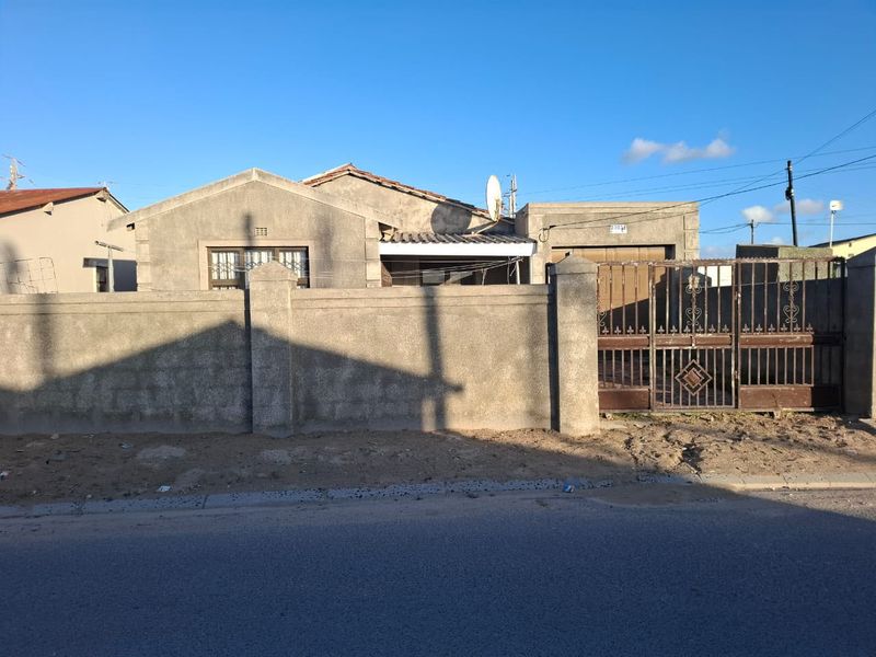 Front elevation of a single-story house featuring a perimeter wall, metal driveway gate, and security bars on windows.
