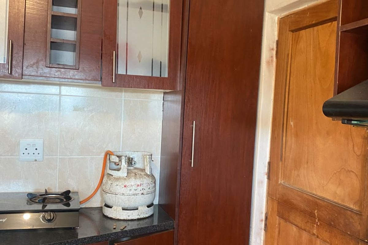 A functional kitchen featuring dark wood cabinetry, granite countertops, a gas hob, and an integrated extractor fan, with a pantry cupboard for storage.