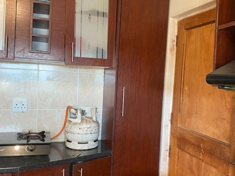 A functional kitchen featuring dark wood cabinetry, granite countertops, a gas hob, and an integrated extractor fan, with a pantry cupboard for storage.