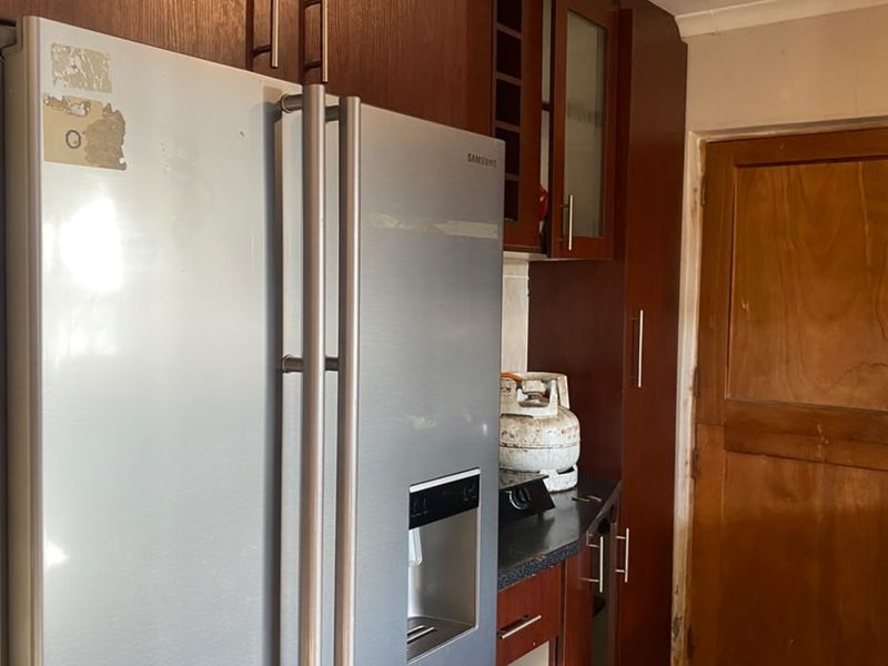 A kitchen area featuring dark wood cabinetry and tiled flooring, showing signs of wear and requiring maintenance or cosmetic updates.