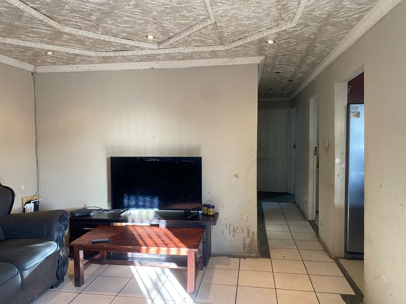 Living area featuring decorative ceiling tiles, recessed lighting, and ceramic floor tiles, requiring cosmetic wall repairs and fresh paint to improve the overall condition.