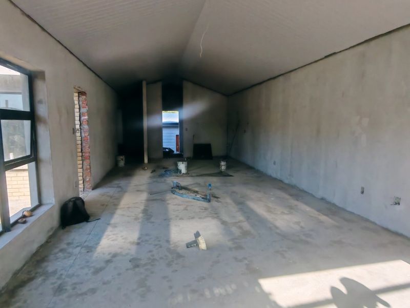 An unfinished open-plan living space featuring vaulted ceilings, exposed brickwork, and large aluminium windows, currently in the construction phase.