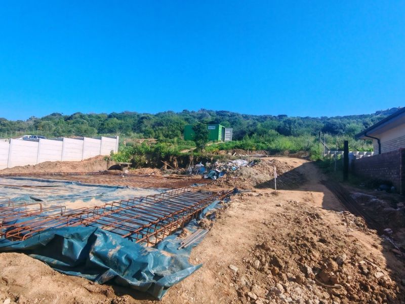 A construction site showing a prepared foundation area with steel reinforcement mesh and damp proofing, bordered by existing boundary walls.