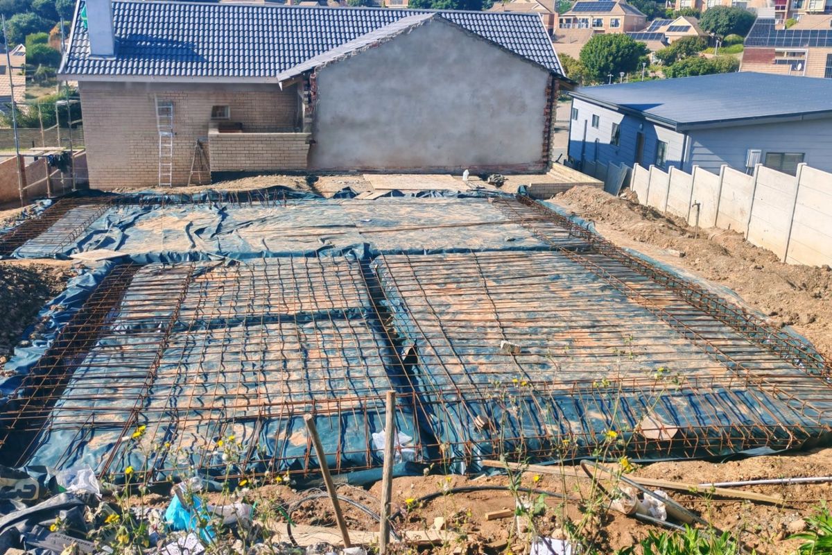 A construction site showing a prepared foundation slab with steel reinforcement mesh and damp proofing, ready for the next phase of building.