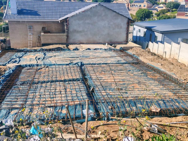 A construction site showing a prepared foundation slab with steel reinforcement mesh and damp proofing, ready for the next phase of building.