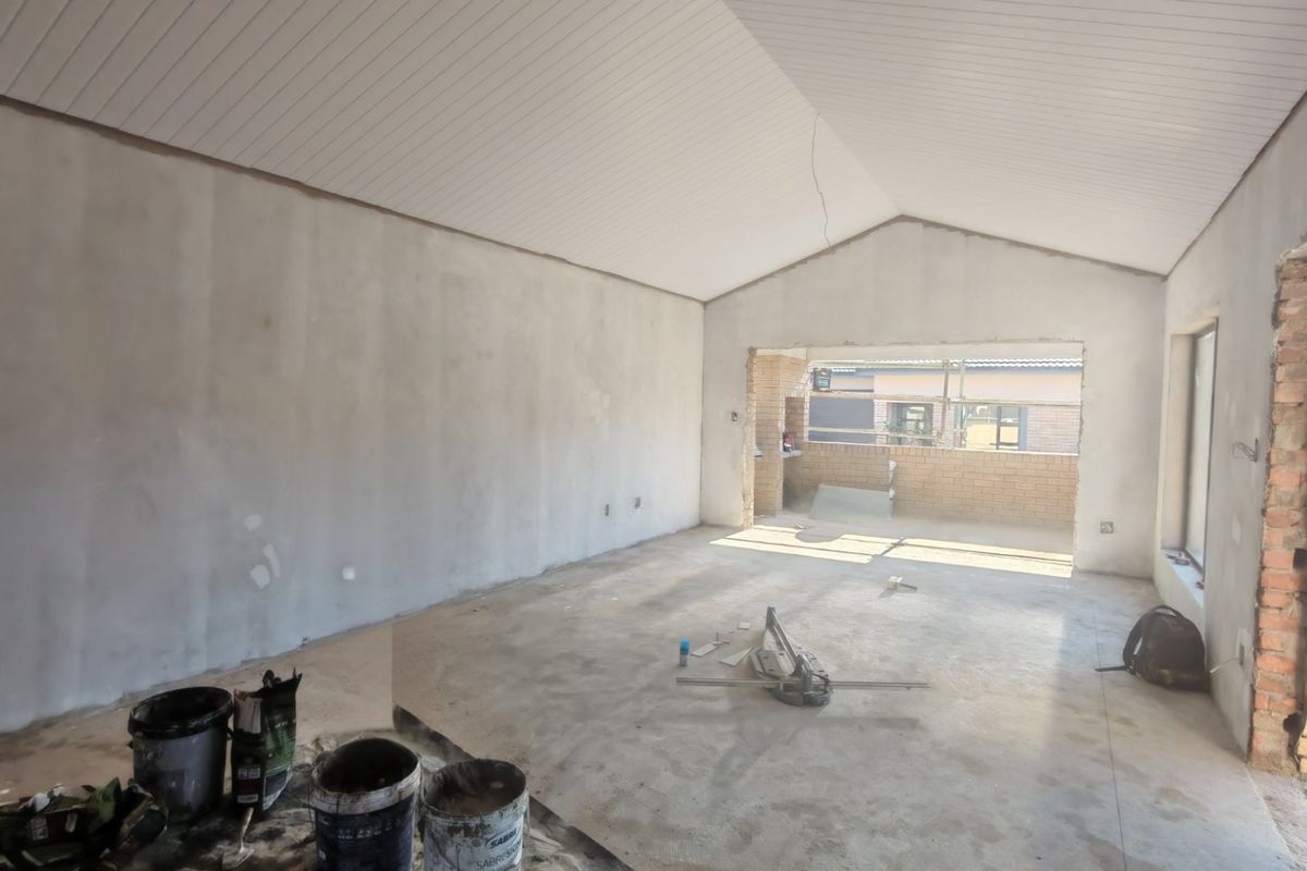 An unfinished living room space featuring a vaulted ceiling, exposed brickwork, and concrete flooring, currently undergoing renovation.